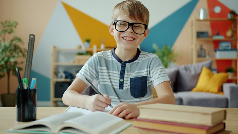 Jongen met bril studeert aan een bureau